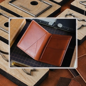 May include: A tan leather card holder with a smooth finish, featuring a vertical pocket on the left side and two horizontal card slots on the right side, with visible stitching along the edges and a folded design resting on a dark grid surface.