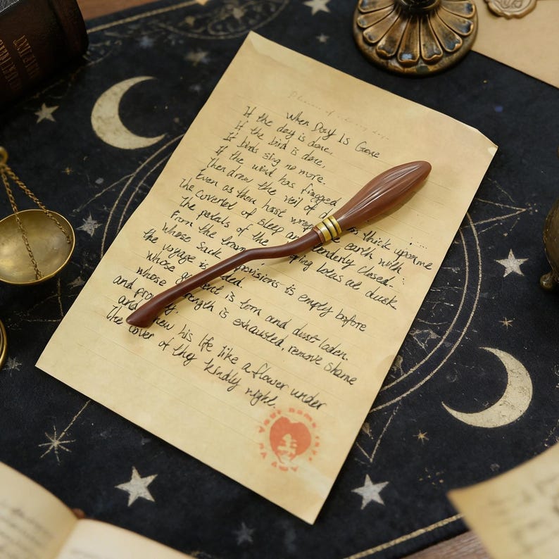 K&ouml;nnte beinhalten: Ein brauner Miniatur-Besen mit goldenen Akzenten liegt auf einem alten Papier mit handschriftlichem Text. Das Papier hat ein rotes Siegel und liegt vor einem dunklen Hintergrund mit Mond- und Sternmotiven.