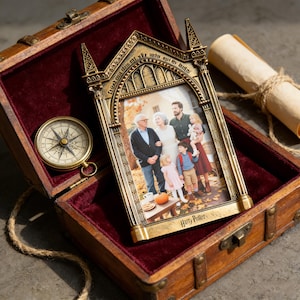 May include: A decorative gold-colored picture frame with a family photo inside, resting in an open wooden treasure chest lined with red velvet. A compass and scroll are also visible. The frame is inscribed with the words "Harry Potter".