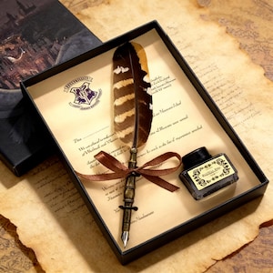 Puede incluir: Un juego de pluma en una caja negra con una cinta marrón. La pluma tiene una pluma marrón y blanca y una punta de metal color bronce. Se incluye un tintero. La caja contiene un papel pergamino con texto y un escudo.