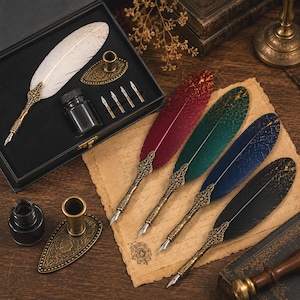 Könnte beinhalten: Ein Set aus Federkielen mit weißen, roten, grünen, blauen und schwarzen Federn mit goldenen Sprenkeln. Jeder Stift hat einen verzierten Metallgriff im Antik-Stil und eine Stahlfeder. Das Set enthält ein schwarzes Tintenfass und Metallhalter.