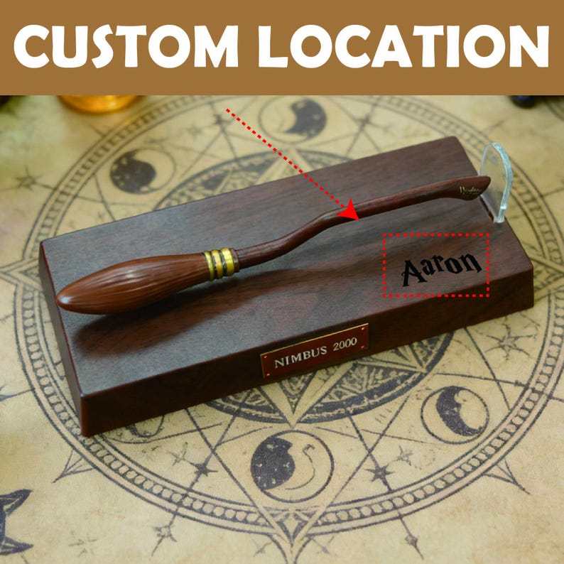 K&ouml;nnte beinhalten: Ein h&ouml;lzerner Besen mit goldenen Akzenten, der auf einem dunkelbraunen Sockel ruht. Der Sockel tr&auml;gt den eingravierten Namen "Aaron" und eine "Nimbus 2000"-Plakette. Oben steht "Custom Location".