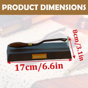 K&ouml;nnte beinhalten: Ein h&ouml;lzerner Nimbus 2000 Besen-Nachbau, 17 cm lang und 8 cm hoch, auf einem dunkelbraunen Sockel. Der Besen hat goldfarbene Akzente und tr&auml;gt den Schriftzug "Nimbus 2000". Die Produktabmessungen sind im Bild angegeben.