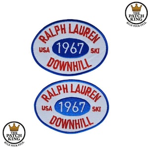 Op de afbeelding: Twee geborduurde patches met een wit ovaal ontwerp, met de tekst "RALPH LAUREN", "USA", "1967" en "DOWNHILL" in rood en blauw. De patches zijn omrand met een blauwe rand. Het logo The Patch King staat in de hoeken.