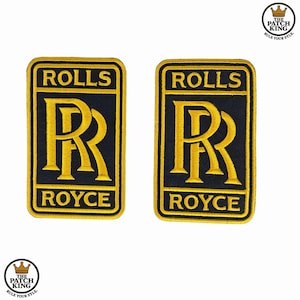 May include: Two embroidered Rolls Royce patches. Each patch has a black background with gold lettering that reads "ROLLS ROYCE" and a gold "RR" emblem. The patches are rectangular with rounded corners.