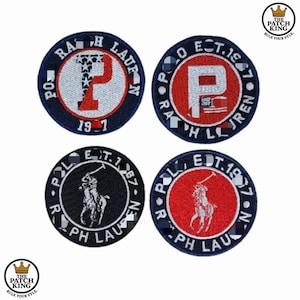 Peut inclure: Quatre écussons brodés circulaires. Deux présentent un "P" rouge à l'intérieur d'un cercle blanc, avec "POLO EST. 1967" et "RALPH LAUREN" sur le bord. Les deux autres ont un joueur de polo ou un "P" avec des étoiles. Le texte "THE PATCH KING" est également visible.