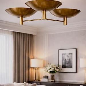 May include: A brass ceiling light fitting featuring three bowl-shaped shades. The fitting is suspended from a central stem and is mounted on the ceiling. The room has a neutral colour palette with a sofa, lamps, and artwork.