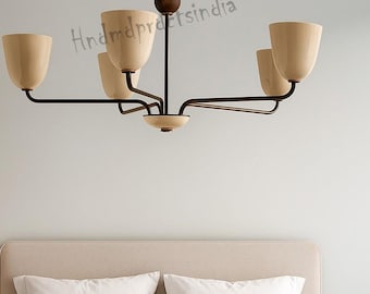 May include: A modern chandelier with five light fixtures. The light fixtures are a light beige color and are shaped like inverted cups. The chandelier has a dark brown metal frame and is suspended from the ceiling. The image shows a bedroom setting.
