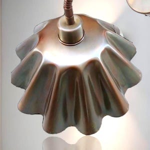 May include: A unique, iridescent metal wall sconce with a ruffled, scalloped shade. The flexible, copper-colored arm curves to hold the light fixture. The sconce is mounted on a white wall, with a reflection of the shade visible.