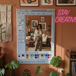 May include: A wall mirror designed to resemble the classic Windows Paint program interface. The mirror is surrounded by a light blue frame with a color palette at the bottom. The text "STAY CREATIVE" is displayed in pink neon. The mirror reflects a room with art and plants.