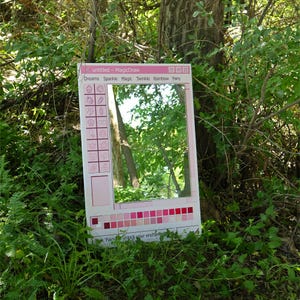 May include: A pink framed mirror with a computer-like interface design. The mirror is surrounded by green foliage and a tree trunk. The text on the frame includes "untitled - MagicDraw", and words like "Dreams", "Sparkle", and "Fairy".