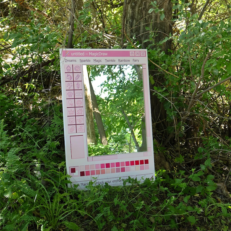 May include: A pink framed mirror with a computer-like interface design. The mirror is surrounded by green foliage and a tree trunk. The text on the frame includes "untitled - MagicDraw", and words like "Dreams", "Sparkle", and "Fairy".
