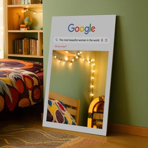 以下が含まれることがあります： 「The most beautiful woman in the world」というクエリが表示されたGoogle検索バーが特徴の額入りプリント。フレーム内の画像は、ストリングライト、ベッド、ジュークボックスのある部屋を映し出しています。Googleのロゴが上部にあります。