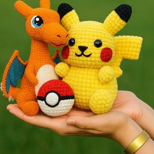 Könnte beinhalten: Gehäkelte Pikachu- und Charizard-Plüschtiere sowie ein Pokéball werden in Händen gehalten. Pikachu ist gelb mit roten Wangen und schwarzen Akzenten. Charizard ist orange mit blauen Flügeln. Der Pokéball ist rot und weiß.