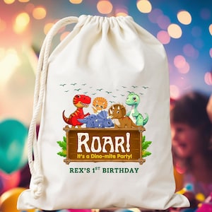 May include: A white drawstring bag featuring a colorful dinosaur-themed design. The design includes various cartoon dinosaurs, the word "ROAR!", and the text "It's a Dino-mite Party!" and "REX'S 1st BIRTHDAY". The bag has a rope drawstring closure.
