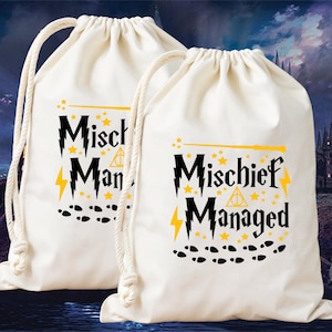 Könnte beinhalten: Zwei cremefarbene Kordelzugbeutel mit dem Text "Mischief Managed" in Schwarz und Gelb. Das Design umfasst Sterne, Blitze und Fußabdrücke. Die Beutel haben weiße Kordelzüge.