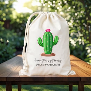 May include: A cream drawstring bag with a green cactus illustration, pink flower, and brown base. The text "Increase things get prickly" and "Emily's Bachelorette" are printed below the cactus design.