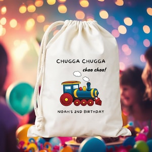 Puede incluir: Una bolsa blanca con cordón y una ilustración de tren colorido con el texto "CHUGGA CHUGGA choo choo!" y "NOAH'S 2ND BIRTHDAY". El tren es azul, amarillo y rojo.