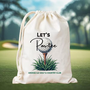 May include: A cream-coloured drawstring bag with a golf-themed design. The design features a golf ball on a tee, with green grass and the words "LET'S Par-tee" in black script. The text "GROSSE ILE GOLF & COUNTRY CLUB" is also printed on the bag.
