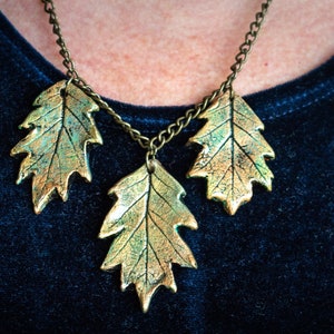 May include: A gold necklace with three leaf pendants. The leaves are a metallic gold color with a green patina.