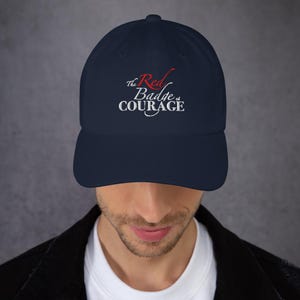 Puede incluir: Gorra de béisbol azul marino con el texto "The Red Badge of Courage" bordado en blanco y rojo. La gorra tiene una visera curva y una correa ajustable. Un accesorio clásico y elegante.