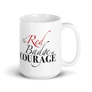 May include: White ceramic mug featuring the text "The Red Badge of Courage" in black and red script. The mug has a curved handle and a glossy finish. A literary-themed gift.