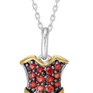 May include: A silver necklace with a dress-shaped pendant. The pendant is adorned with red and blue gemstones, and gold detailing. The necklace chain is silver.