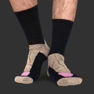 May include: Novelty socks featuring a dark blue upper and a beige foot design. The foot design includes a pink toe and a graphic pattern. The socks are ribbed and reach the mid-calf.