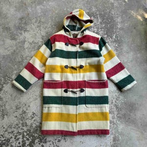 May include: A multi-coloured striped duffel coat with a hood. The coat has horizontal stripes in red, green, yellow, and white. It features a toggle closure and two front pockets. The coat is approximately 102 cm long.