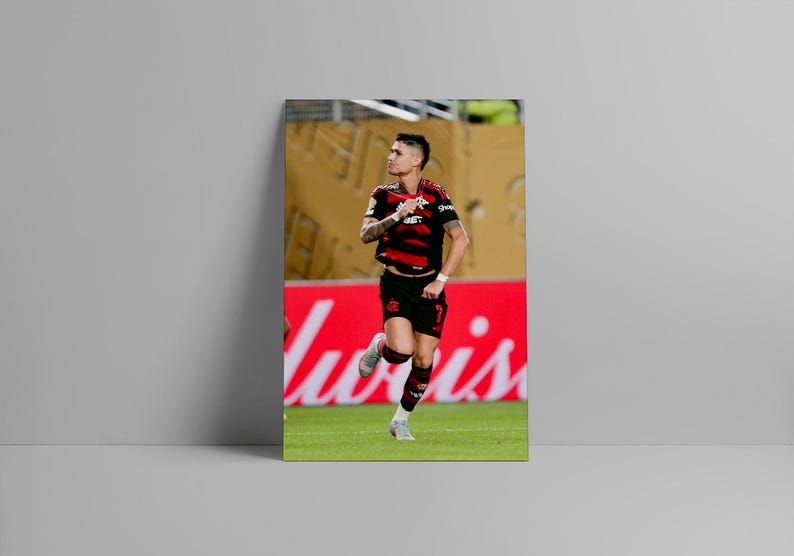 Puede incluir: Impresi&oacute;n enmarcada de un jugador de f&uacute;tbol con camiseta a rayas negras y rojas y pantalones cortos negros, corriendo sobre un campo verde. El fondo incluye un letrero rojo con texto blanco y una pared amarilla.