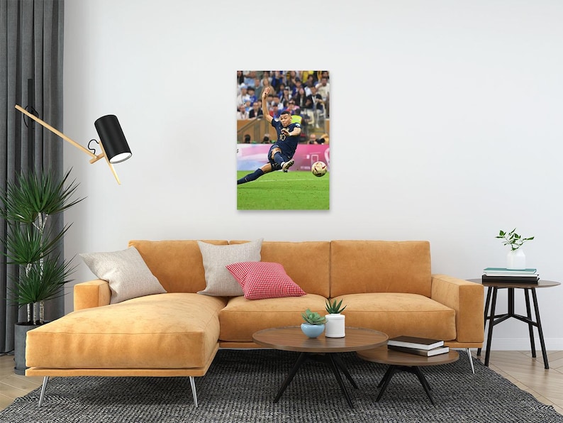 May include: A framed print of a soccer player in a blue uniform kicking a soccer ball on a green field. The player is mid-kick, with the ball in front of them. The background shows a crowd of spectators.