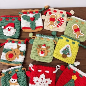 Könnte beinhalten: Eine Sammlung handgefertigter gehäkelter Weihnachtsgeschenktüten in verschiedenen Farben. Jede Tasche hat ein anderes festliches Design, darunter der Weihnachtsmann, ein Rentier, ein Schneemann, ein Weihnachtsbaum und ein Schneeflocke. Ideal für kleine Geschenke.