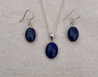 May include: A jewellery set comprising a silver chain necklace with a matching pendant and a pair of earrings. Each piece features a dark blue oval stone set in a silver bezel. The earrings have a hook closure.