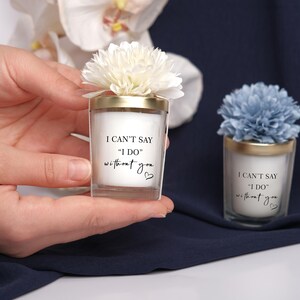 May include: Two small, clear glass candles with gold rims and floral accents. The candles have the text "I CAN'T SAY 'I DO' without you" printed on them. One candle has a white flower, the other a blue flower.