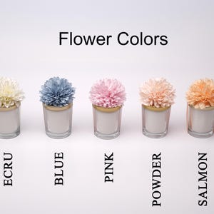 May include: Five glass candle holders with different colored flower arrangements: ecru, blue, pink, powder, and salmon. Each candle holder has a gold rim and is labeled with the flower color.