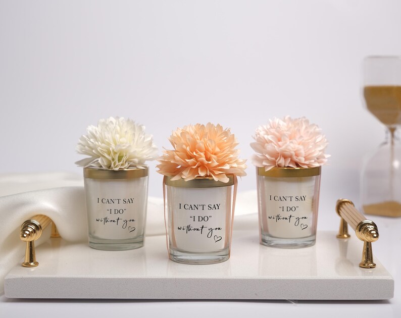 May include: Three glass candle holders with gold rims and floral accents, arranged on a white tray with gold handles. Each candle has the text "I CAN'T SAY 'I DO' without you" printed on it, with a small heart symbol.