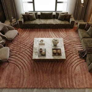 May include: An overhead view of a living room with a large, patterned rug in shades of rose and brown. The room features a sectional sofa, two armchairs, and a marble coffee table. The sofa and chairs are upholstered in a muted green fabric.