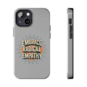 May include: A gray phone case with the words "EMBRACE RADICAL EMPATHY" in a retro design. The text is in white and orange, with a sunburst design around the words. The case has a black camera and button details.