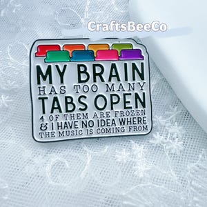 Könnte beinhalten: Rechteckiger Emaille-Pin mit dem Text "MY BRAIN HAS TOO MANY TABS OPEN". Der Pin hat farbige Registerkarten oben und den Text "4 OF THEM ARE FROZEN & I HAVE NO IDEA WHERE THE MUSIC IS COMING FROM".