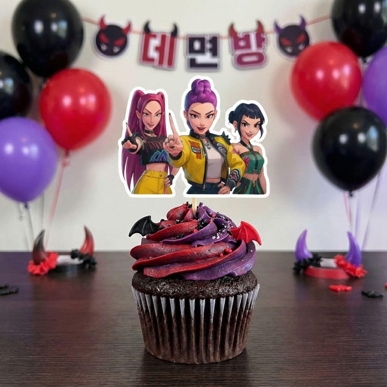 May include: A decorated cupcake with red and purple frosting, bat-shaped decorations, and a cartoon image of three women. The background includes red, black, and purple balloons, and a banner with Korean text.