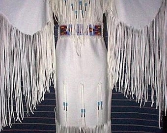 May include: A white dress with long fringed sleeves and a fringed hem. The dress features a V-neckline with fringe and small blue and turquoise accents. A colourful beaded belt cinches the waist.