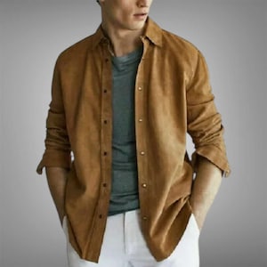 Peut inclure: Une chemise boutonnée marron à manches longues, en matière effet daim, avec un col. Elle est portée sur un t-shirt gris et associée à un pantalon blanc. Style classique et décontracté.