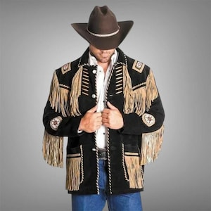 Puede incluir: Chaqueta de ante negra con flecos color canela y costuras decorativas. La chaqueta presenta un cuello con muescas, cierre de botones y parches decorativos. Se lleva un sombrero de vaquero marrón con una banda blanca.