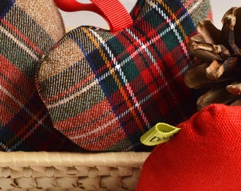 Könnte beinhalten: Nahaufnahme von herzförmigen Stoffornamenten mit Karomuster in einem Weidenkorb. Die Ornamente weisen rot-, grün- und weiß karierte Muster mit roten Schleifen auf. Ein roter Stoffbeutel und ein Tannenzapfen sind ebenfalls zu sehen.