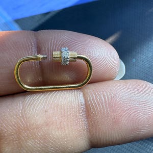 以下が含まれることがあります： ネジ留め式の長方形の金色の留め金。留め金の中央の円筒部分は、小さな透明な宝石で飾られています。ジュエリーやアクセサリー用に設計されています。