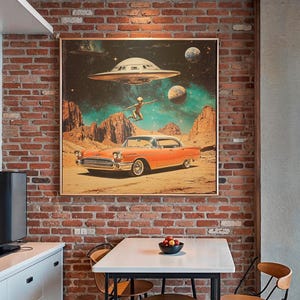 May include: A framed art print showing a vintage car in a desert scene with a UFO and an alien figure. The artwork uses a mid-century modern style, with orange, teal, and brown tones. The print is displayed on a brick wall.