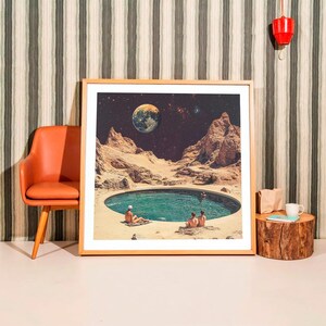 a framed picture of a desert landscape with a small pool of water in the center, surrounded by mountains and a large planet in the sky.