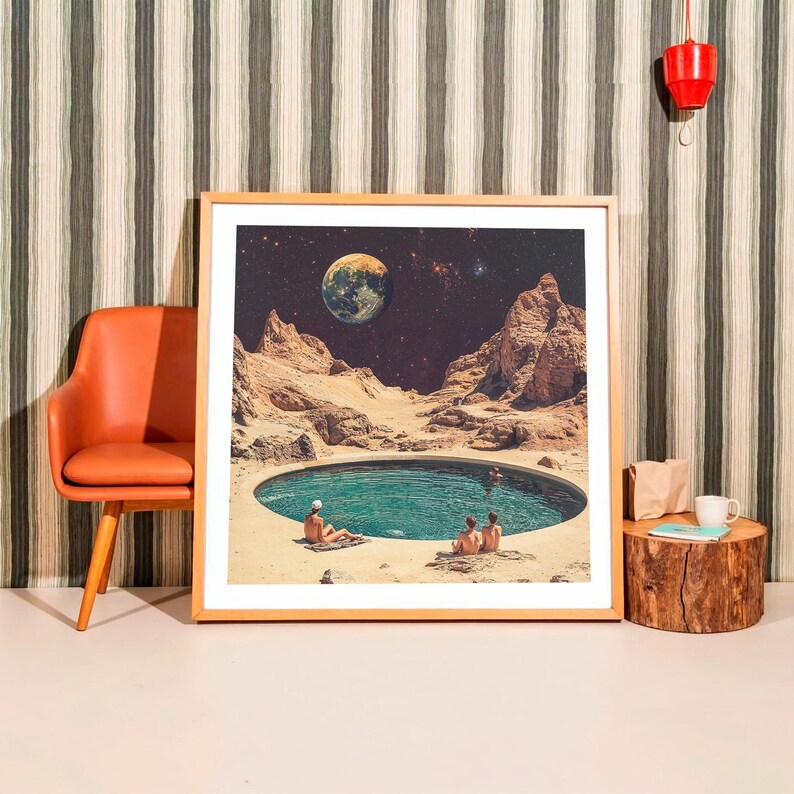 a framed picture of a desert landscape with a small pool of water in the center, surrounded by mountains and a large planet in the sky.