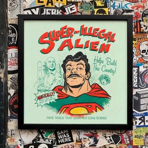 May include: Framed art print with the words "SUPER-ILLEGAL ALIEN" in red and green. The image features a superhero-like figure with a mustache and a Superman-style logo. The text reads "Helps Build This Country!" and "Pays Taxes That Corporations Dodge."