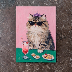 May include: A painting on a pink background featuring a fluffy brown tabby cat wearing black sunglasses and a small purple crown. The cat sits at a green table with a red drink in a glass with a striped straw and two plates of small pastries.